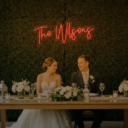 Photo of the 'Wedding Last Names Custom Neon Sign V4' neon sign glowing in golden yellow against a styled interior wall.