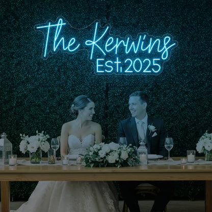 Photo of the 'Wedding Last Names Custom Neon Sign V5' neon sign glowing in ice blue against a styled interior wall.
