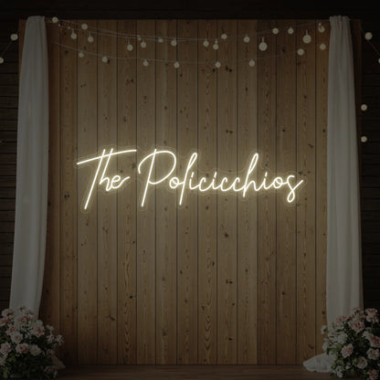 Photo of the 'Wedding Last Names Custom Neon Sign V7' neon sign glowing in warm white against a styled interior wall.