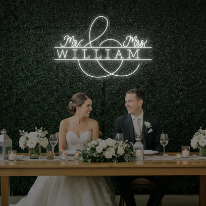 Photo of the 'Wedding Last Names Custom Neon Sign V3' neon sign glowing in cool white against a styled interior wall.