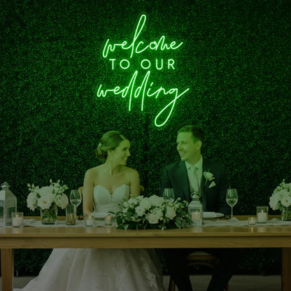  'Welcome To Our Wedding' neon sign glowing in green against a styled interior wall.