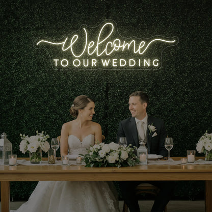  'Welcome To Our Wedding' neon sign glowing in warm white against a styled interior wall.