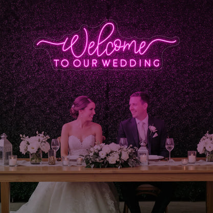  'Welcome To Our Wedding' neon sign glowing in light pink against a styled interior wall.