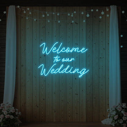 'Welcome To Our Wedding' neon sign glowing in ice blue against a styled interior wall.