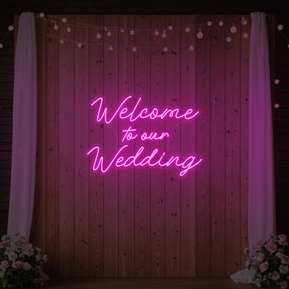  'Welcome To Our Wedding' neon sign glowing in deep pink against a styled interior wall.