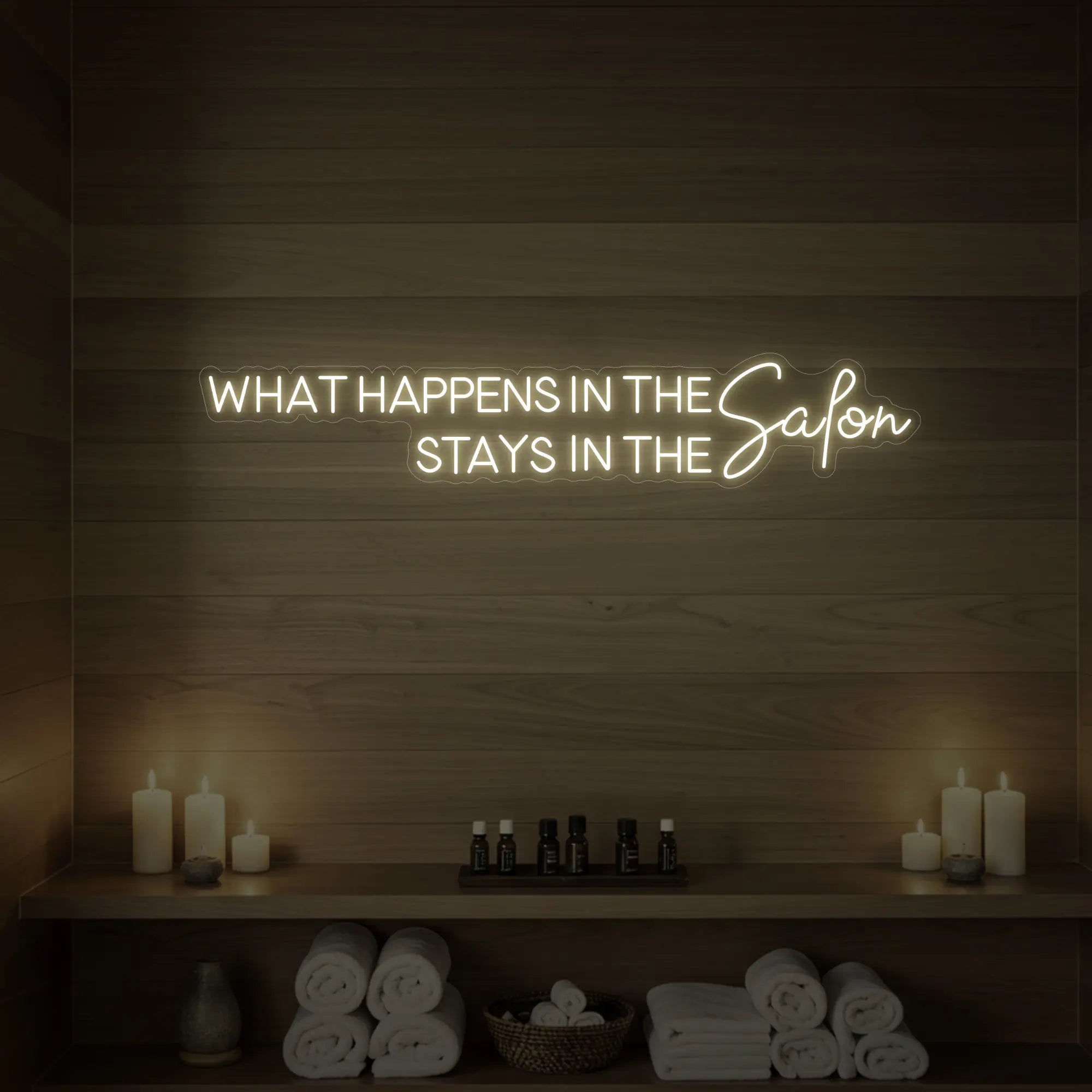 Photo of the 'WHAT HAPPENS IN THE SALON STAYS IN THE SALON' neon sign glowing in warm white against a styled interior wall.