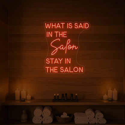 Photo of the 'WHAT IS SAID IN THE SALON STAY IN THE SALON' neon sign glowing in golden yellow against a styled interior wall.
