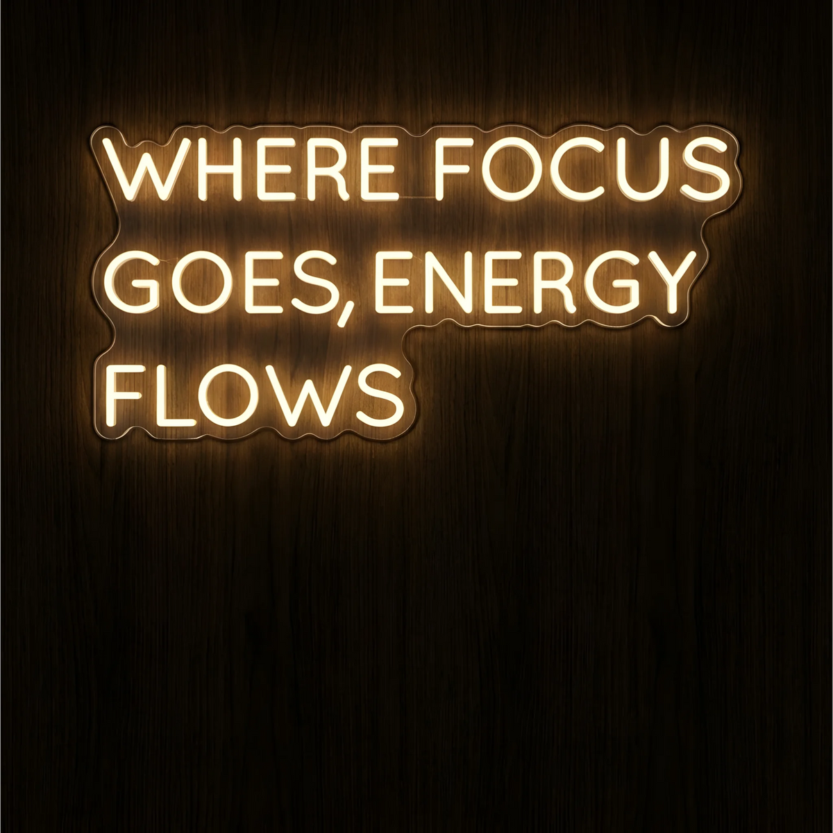 Where Focus Goes, Energy Flows LED Neon Sign in warm white lettering on clear acrylic against a dark wood background, suited to home offices and creative workspaces.