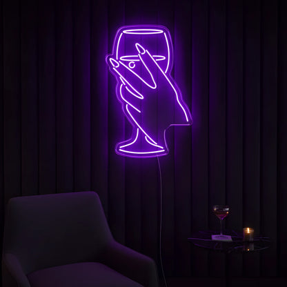 Photo of the 'Wine in Hand Version 1' neon sign glowing in purple against a cozy wine-inspired wall.