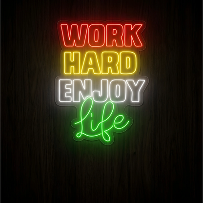 “WORK HARD ENJOY Life” LED Neon Sign with red, yellow, white, and green lettering on clear acrylic backing against a dark wood background, suited to home offices, workspaces, and creative studios.