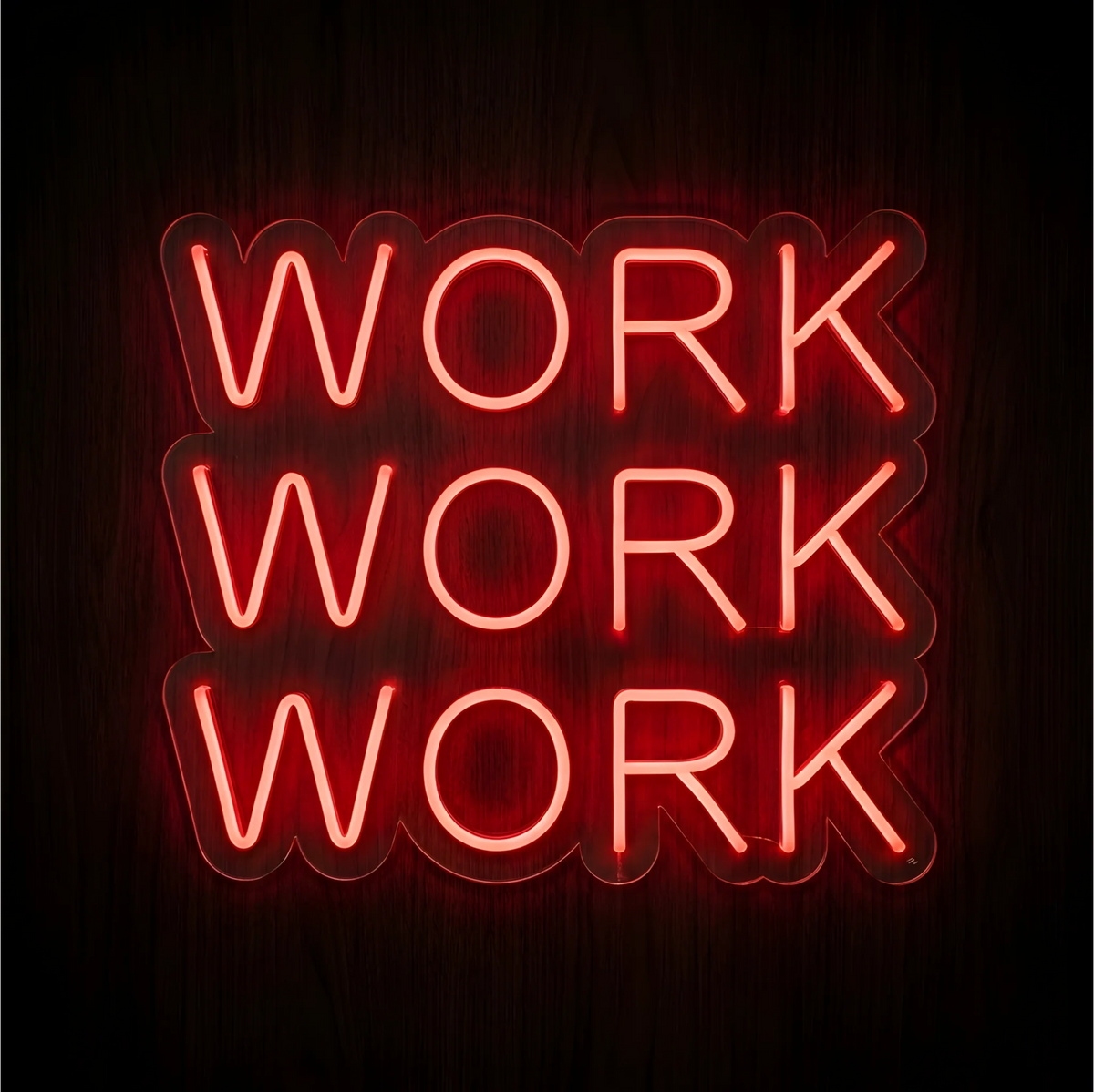 Work Work Work LED Neon Sign with three stacked lines of bright red uppercase lettering on clear acrylic backing, displayed against a dark wood background for office and workspace decor.