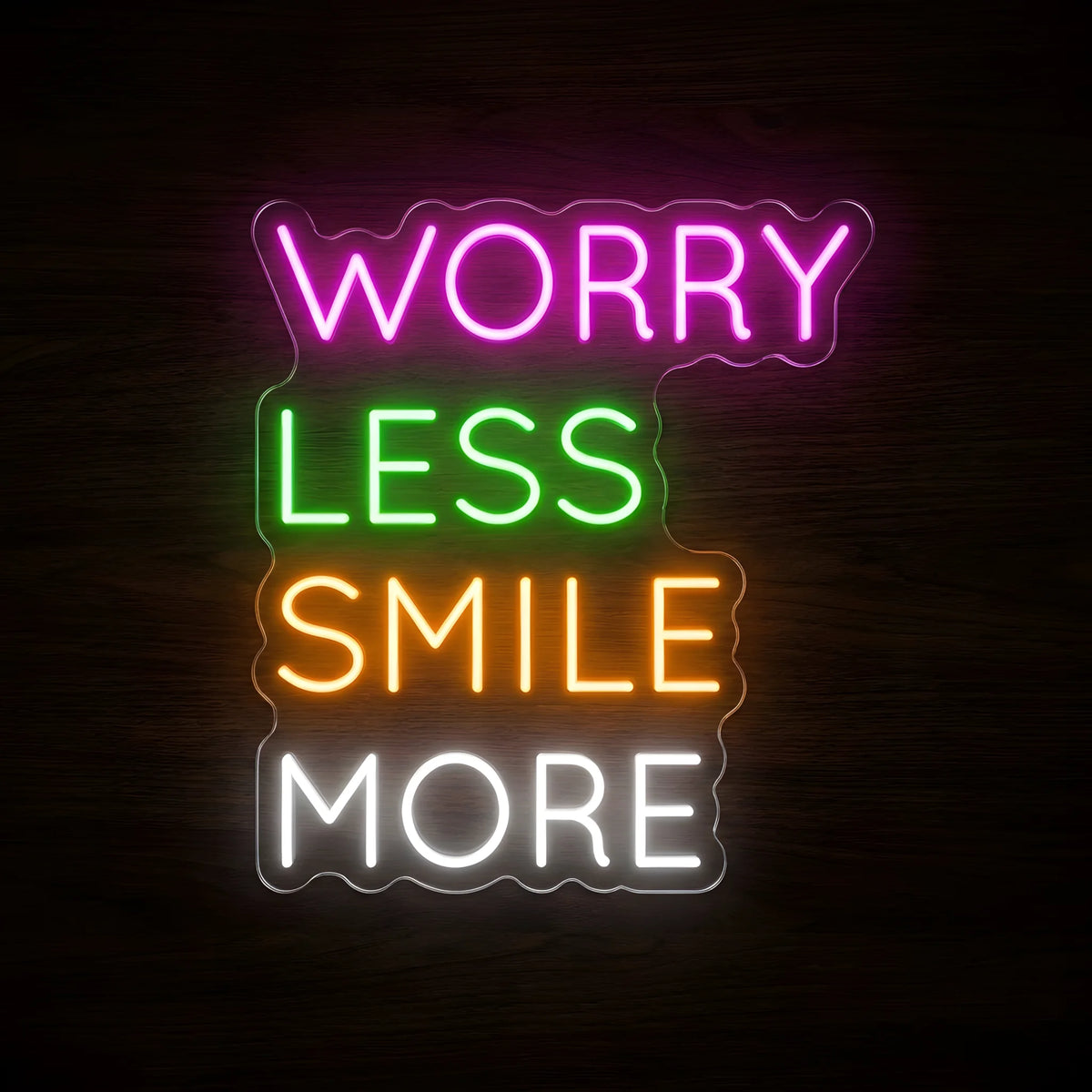Worry Less Smile More LED neon sign featuring pink WORRY, green LESS, orange SMILE, and white MORE lettering on clear acrylic backing against a dark wooden wall.
