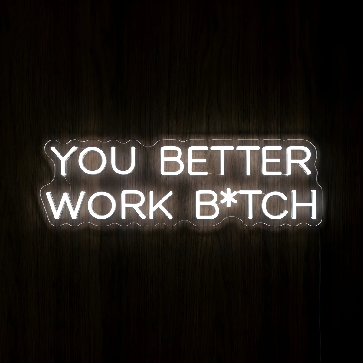 “You Better Work B*TCH” LED Neon Sign glowing in bright white uppercase lettering across two lines on clear acrylic against a dark wood background, suited to home offices and creative workspaces.