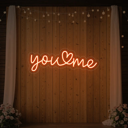  'You Heart Me' neon sign glowing in golden yellow against a styled interior wall.