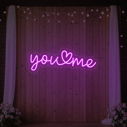 'You Heart Me' neon sign glowing in deep pink against a styled interior wall.