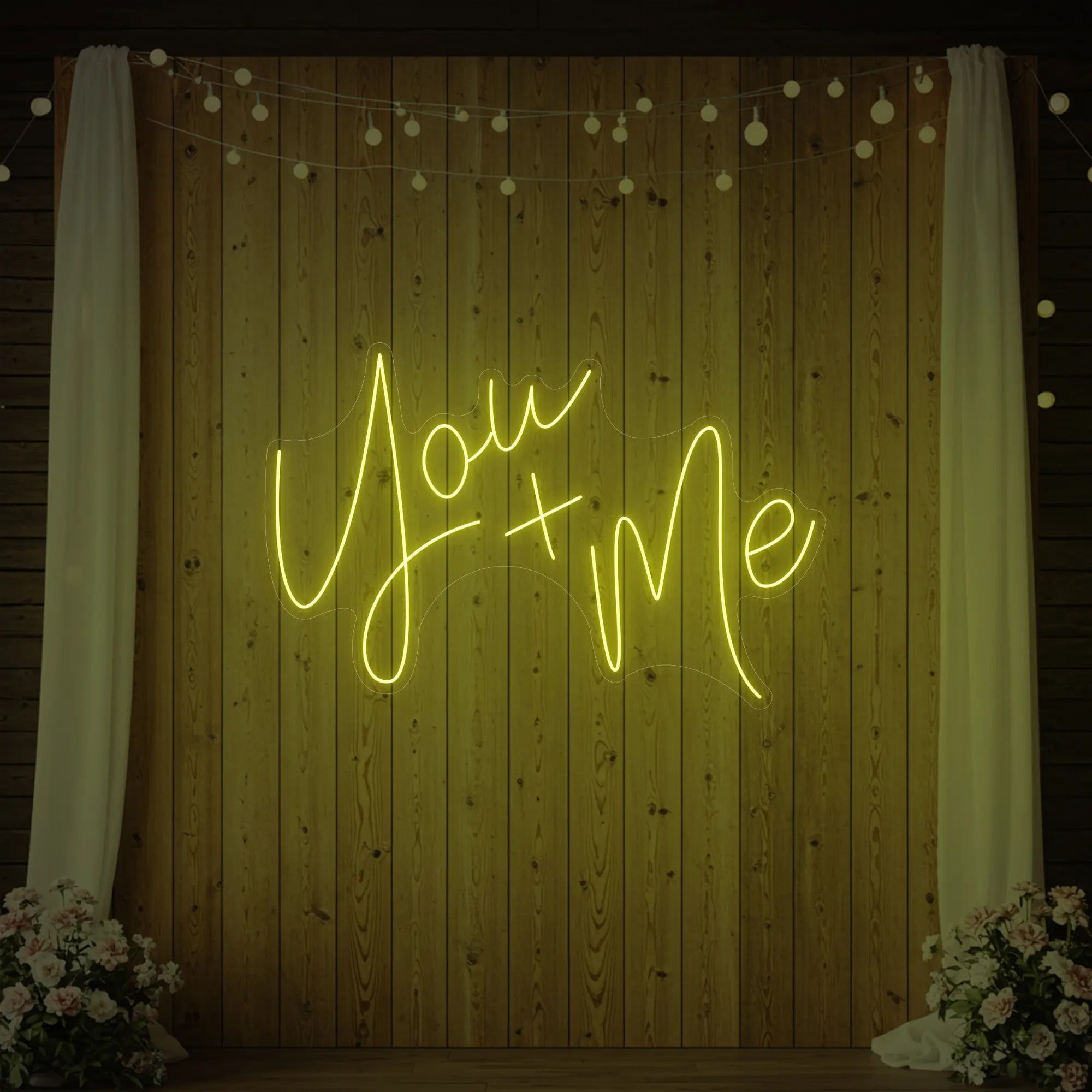 'You + Me' neon sign glowing in lemon yellow against a styled interior wall.