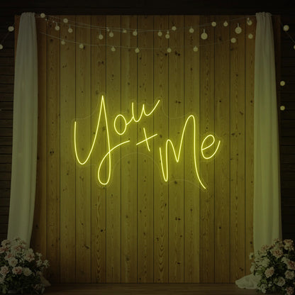  'You + Me' neon sign glowing in lemon yellow against a styled interior wall.