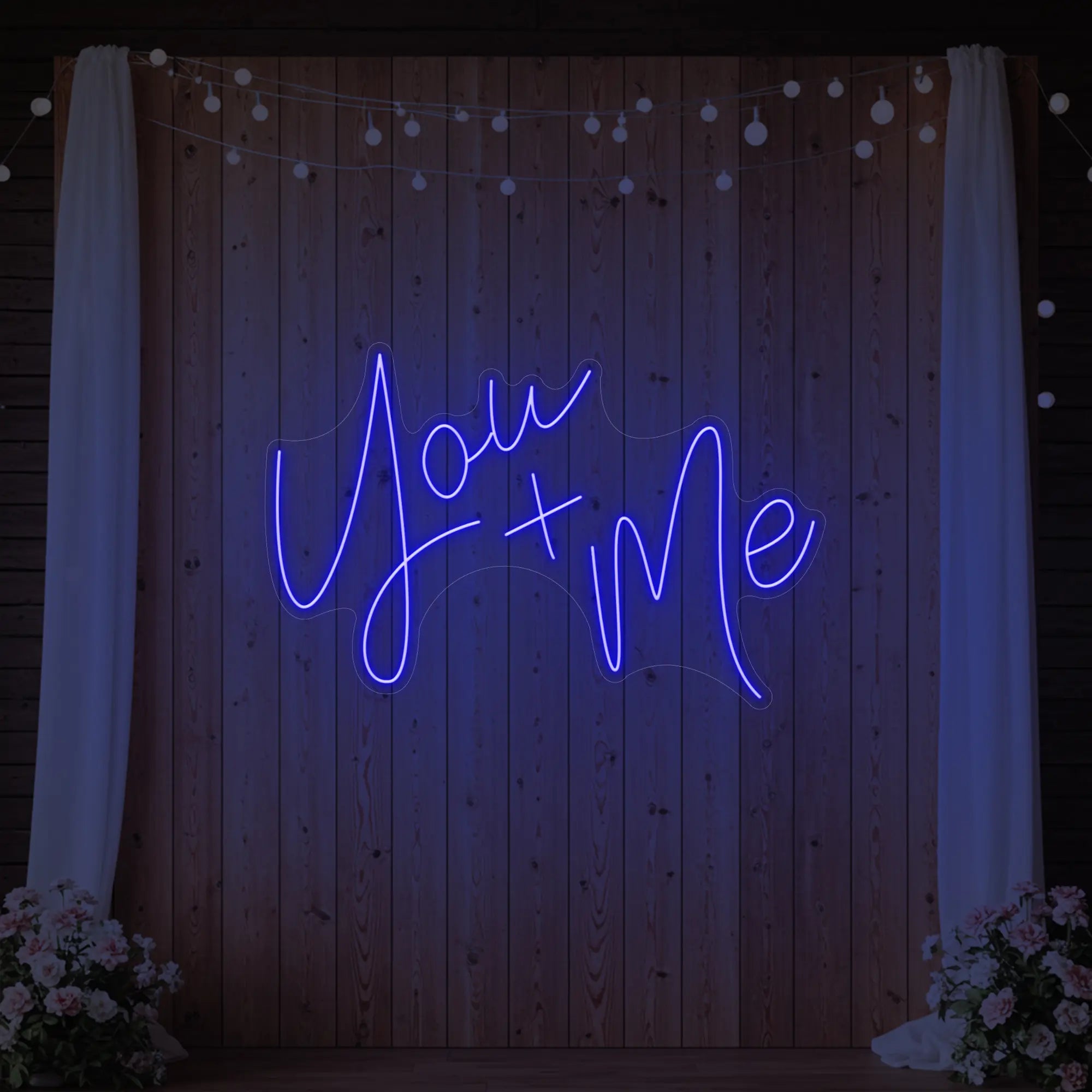  'You + Me' neon sign glowing in deep blue against a styled interior wall.