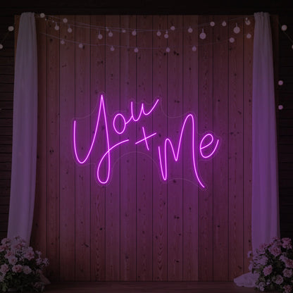 'You + Me' neon sign glowing in deep pink against a styled interior wall.